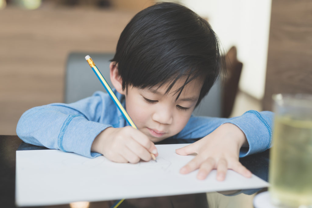 Cute Asian child writing on white paper